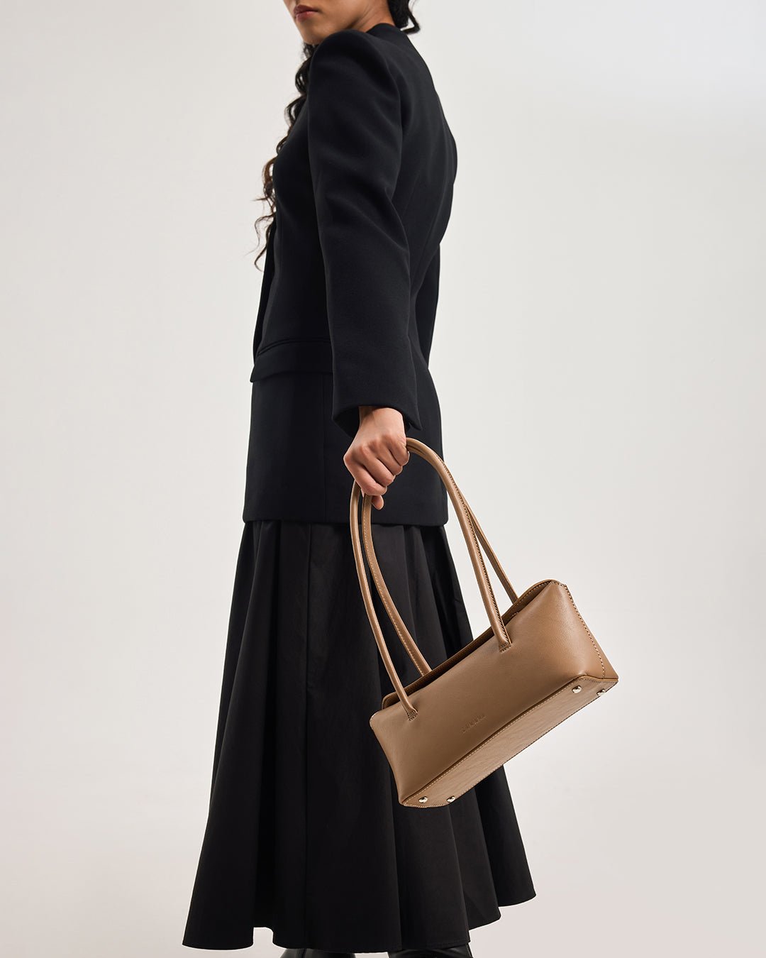 Caramel mini tote bag with rounded handles and front logo, held to the side