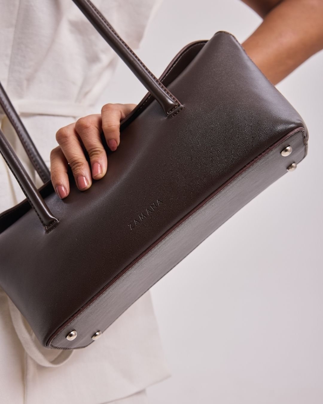 Dark brown leather-look tote bag with two top handles and metal-look button details