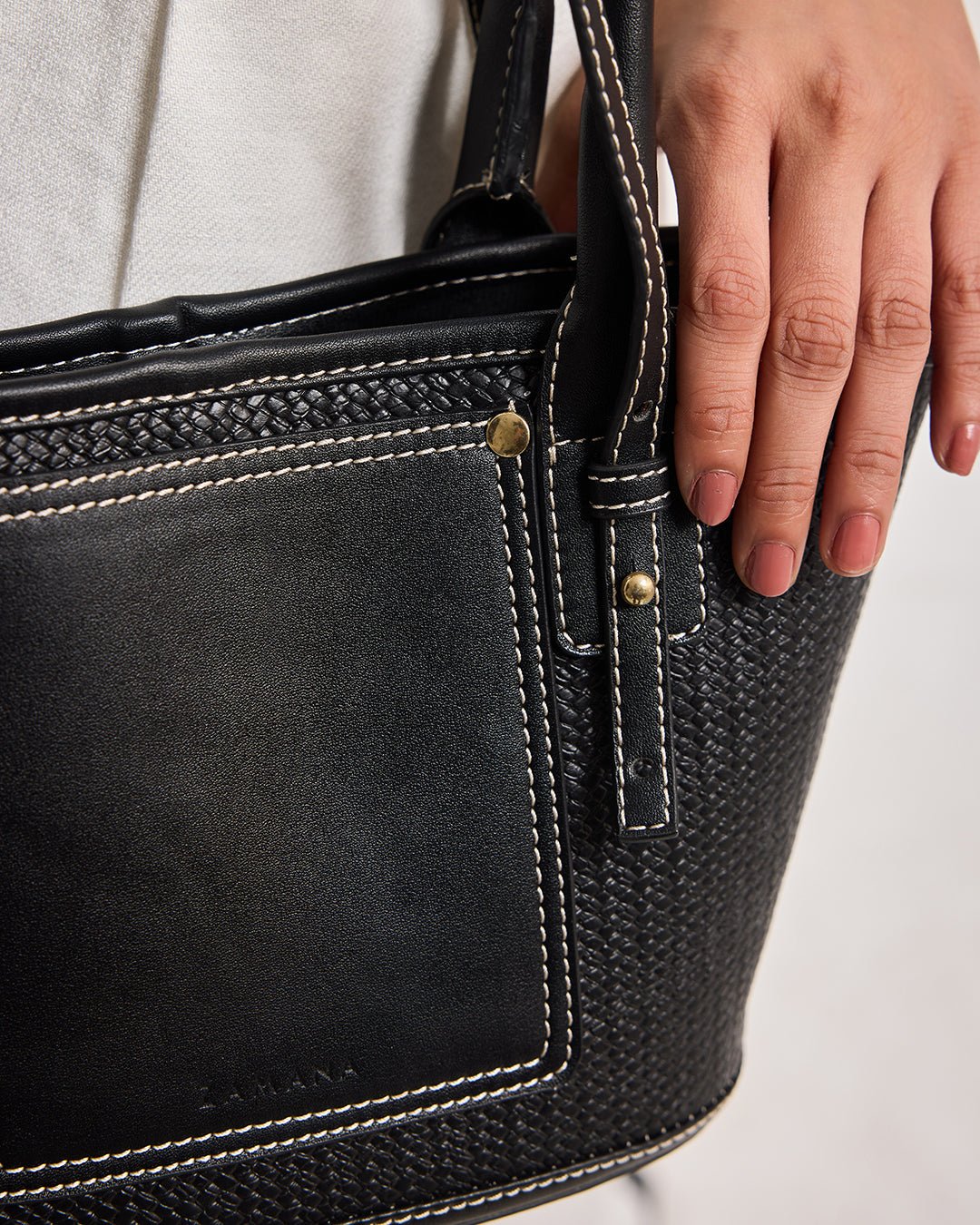Black woven handbag with front pocket, contrast stitching, and gold-tone rivets