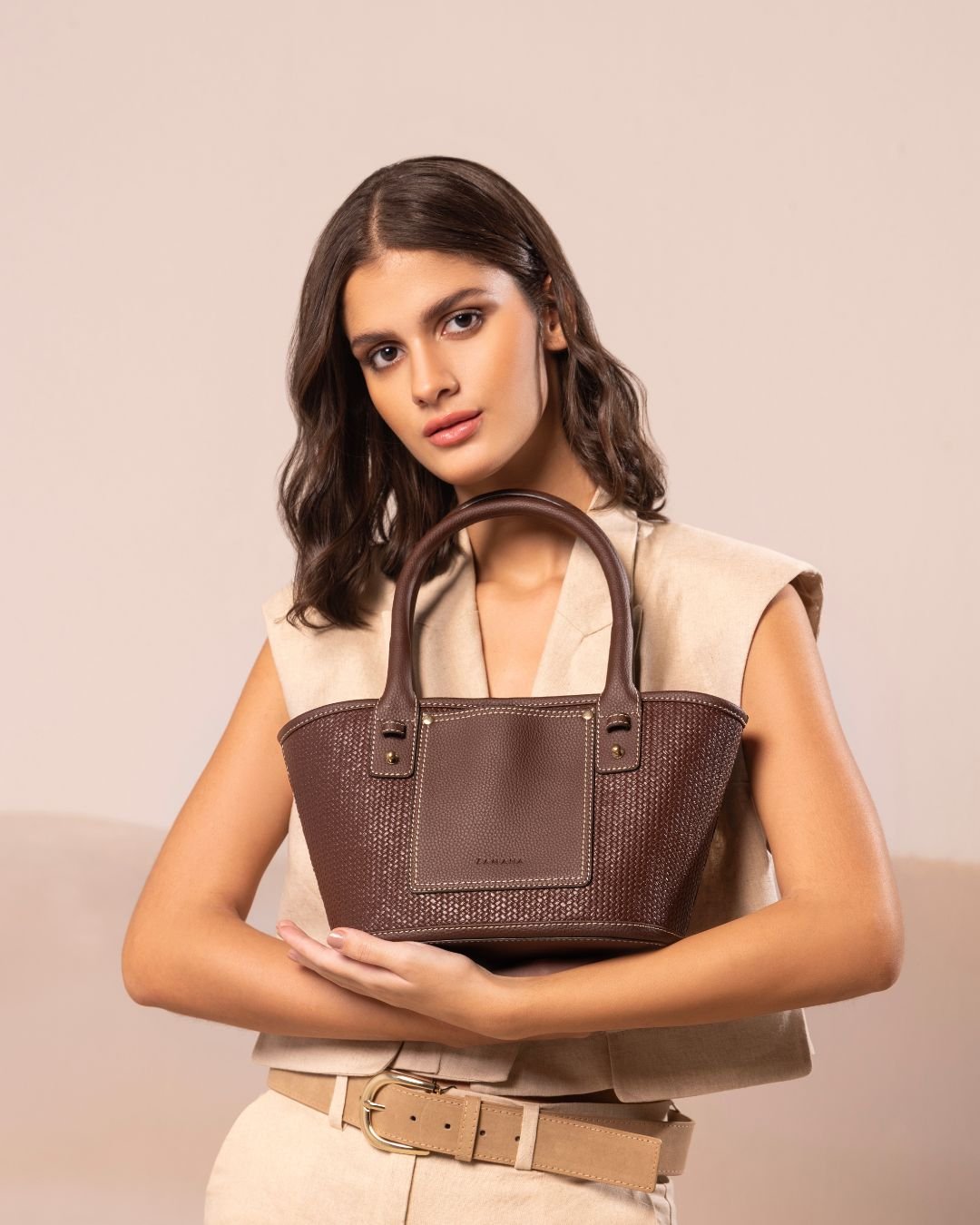 Brown woven tote bag with top handles and front logo patch, gold-tone hardware